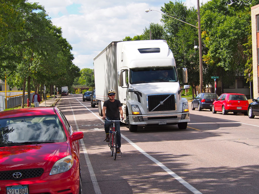 Truck navigates a local street alongside a bicyclist